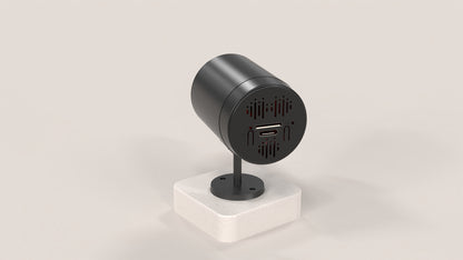 Black cylindrical device with ports on a white stand against a light gray background